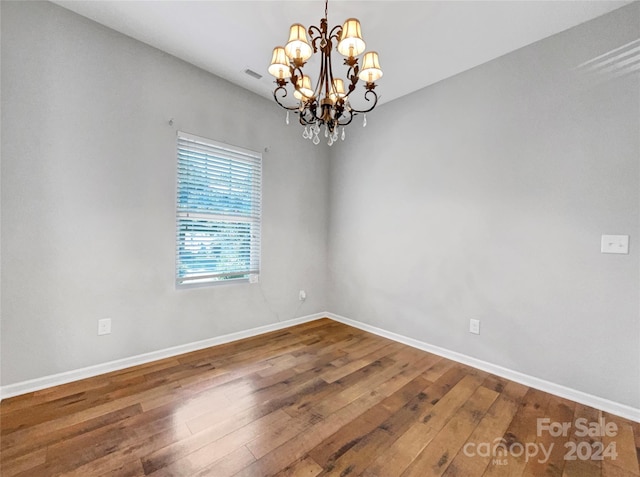 spare room with a notable chandelier, baseboards, and hardwood / wood-style floors