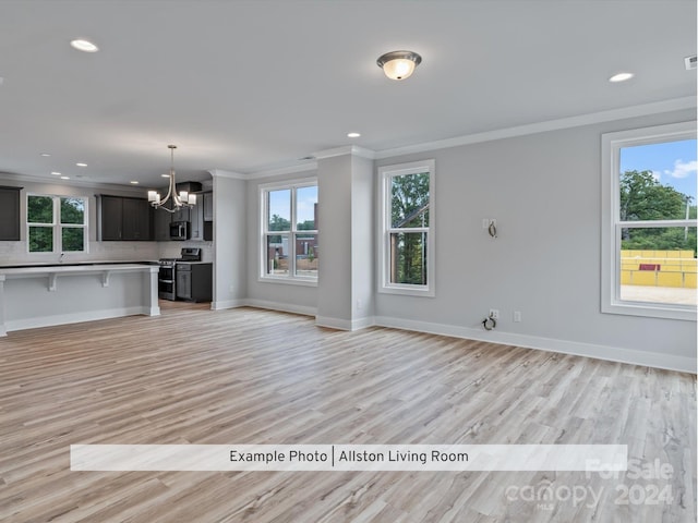 unfurnished living room featuring ornamental molding, an inviting chandelier, plenty of natural light, and light hardwood / wood-style floors