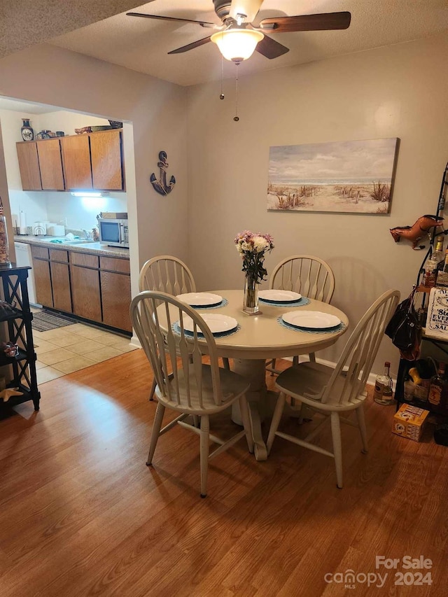 dining space featuring light wood-type flooring, ceiling fan, and a textured ceiling