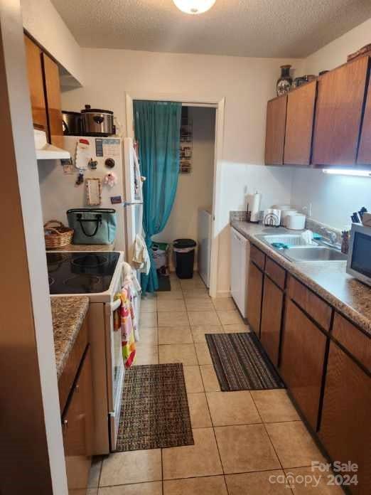 kitchen featuring light tile patterned floors, a textured ceiling, sink, and white appliances