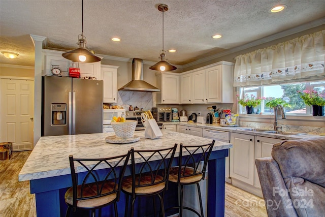 kitchen featuring hanging light fixtures, stainless steel appliances, white cabinetry, wall chimney range hood, and a kitchen island