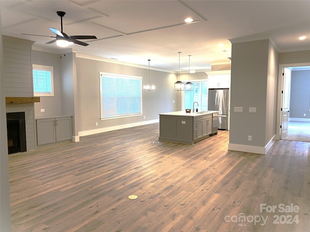 kitchen with sink, a center island with sink, a fireplace, stainless steel refrigerator, and hanging light fixtures