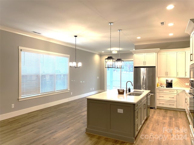 kitchen featuring appliances with stainless steel finishes, decorative light fixtures, hardwood / wood-style flooring, white cabinetry, and an island with sink