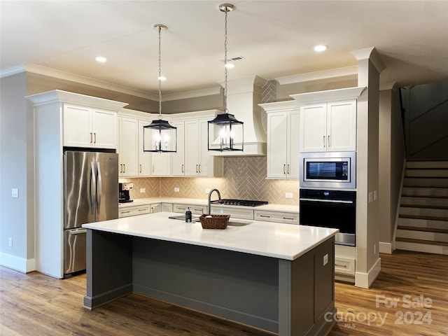 kitchen with ornamental molding, appliances with stainless steel finishes, a center island with sink, white cabinets, and hardwood / wood-style flooring