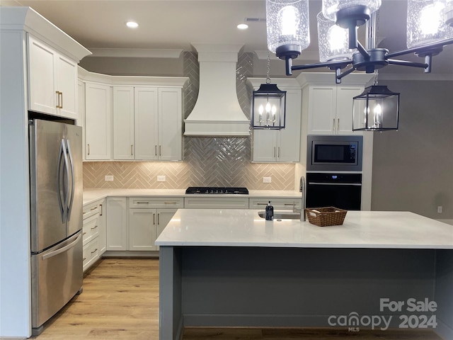 kitchen featuring black appliances, hanging light fixtures, light wood-type flooring, custom range hood, and white cabinetry