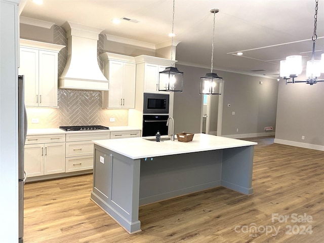 kitchen with white cabinetry, stainless steel appliances, a kitchen island with sink, custom range hood, and light wood-type flooring