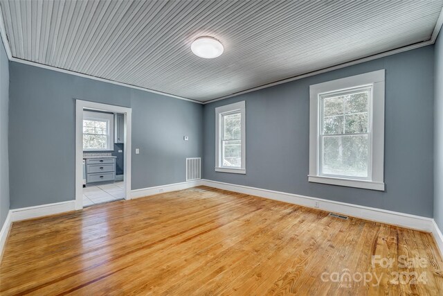 empty room featuring light wood-type flooring, a wealth of natural light, and ornamental molding