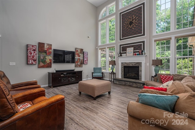 living room featuring a stone fireplace, baseboards, a towering ceiling, and wood finished floors