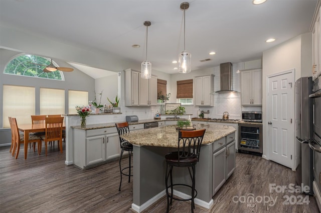 kitchen featuring appliances with stainless steel finishes, wine cooler, a kitchen island, and wall chimney exhaust hood