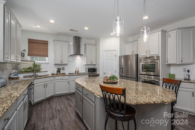 kitchen with appliances with stainless steel finishes, sink, wall chimney range hood, a center island, and hanging light fixtures