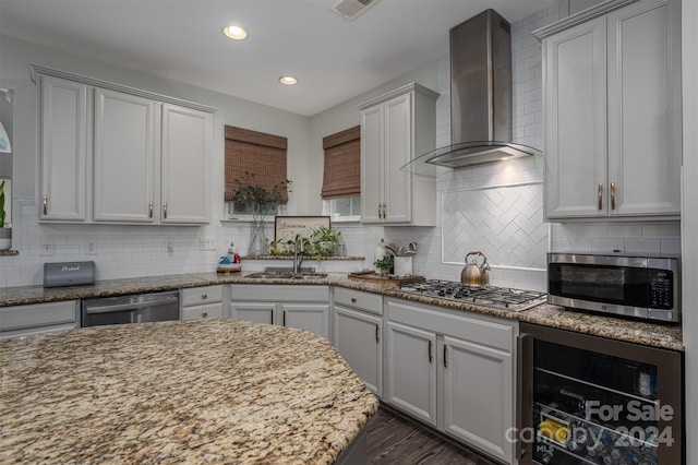 kitchen featuring wall chimney range hood, light stone countertops, beverage cooler, stainless steel appliances, and a sink