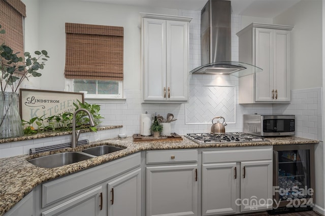 kitchen with wine cooler, decorative backsplash, appliances with stainless steel finishes, wall chimney exhaust hood, and a sink