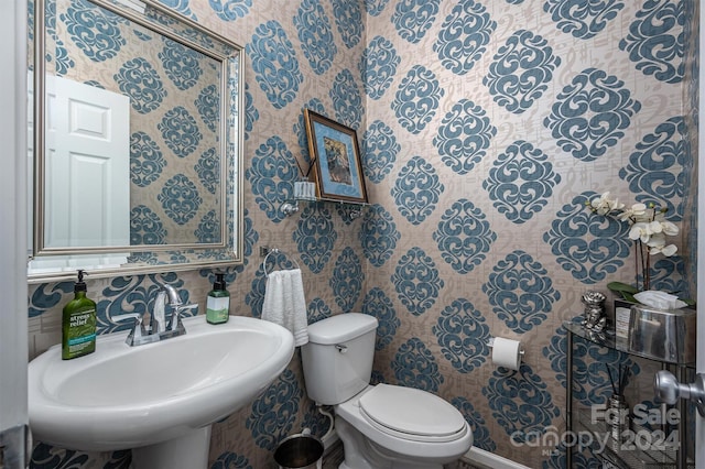 half bathroom with wallpapered walls, toilet, and a sink