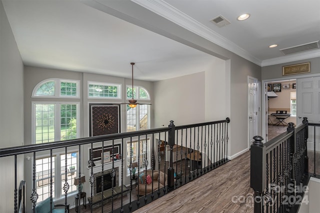 hallway featuring baseboards, wood finished floors, visible vents, and ornamental molding