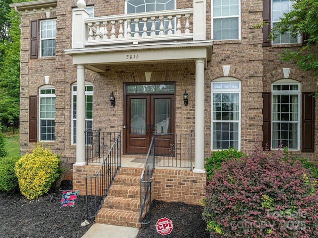 view of exterior entry featuring french doors, a balcony, and brick siding