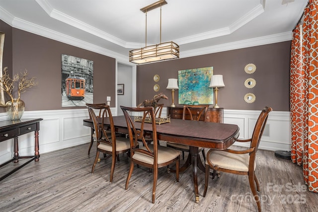 dining area with wood-type flooring, a raised ceiling, and crown molding