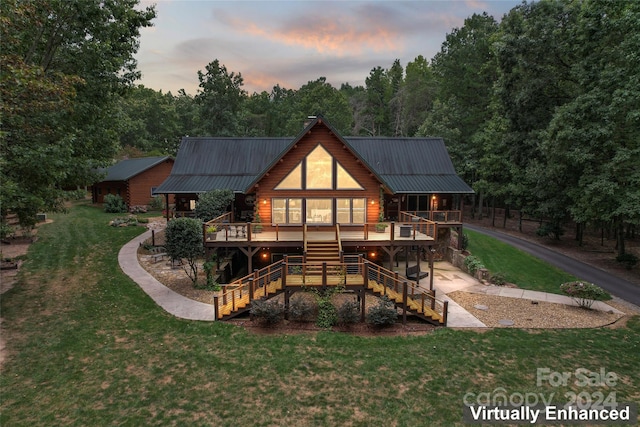 back house at dusk featuring a deck and a lawn