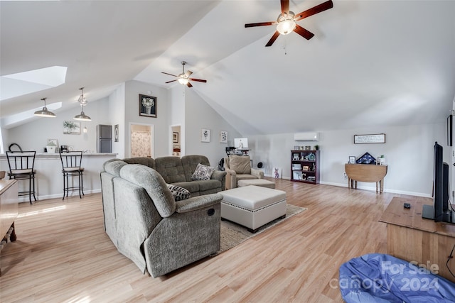 living room featuring ceiling fan, a wall unit AC, vaulted ceiling with skylight, and light hardwood / wood-style floors