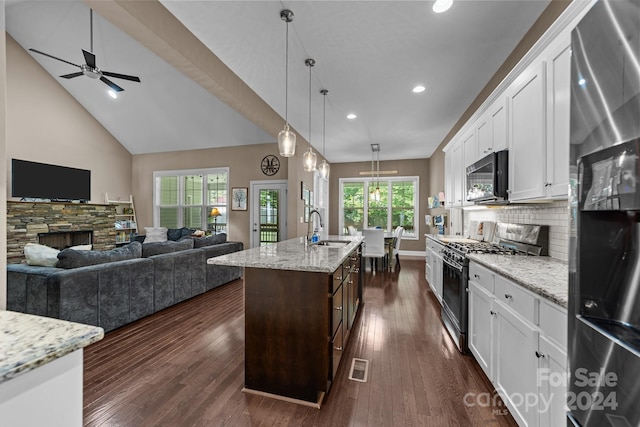 kitchen with a fireplace, gas range oven, stainless steel fridge, an island with sink, and ceiling fan