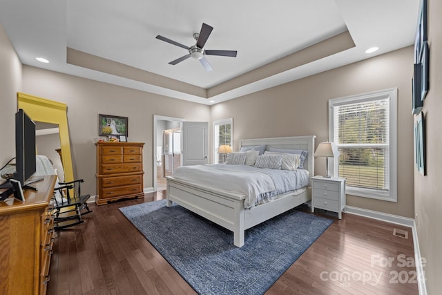 bedroom with ensuite bath, a raised ceiling, ceiling fan, and dark hardwood / wood-style floors