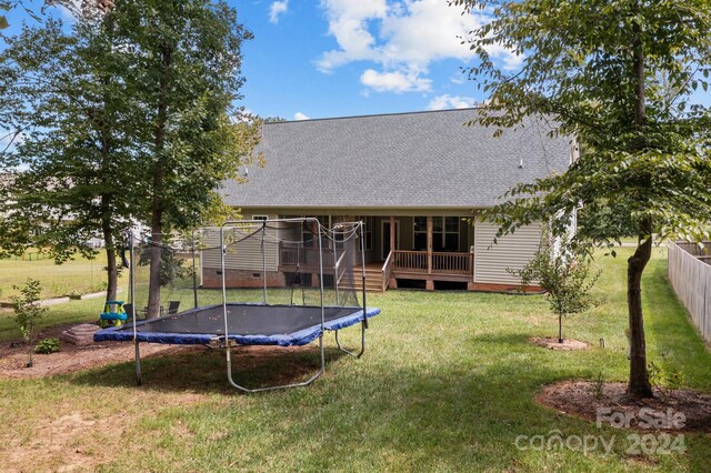 back of house with a yard, a wooden deck, and a trampoline