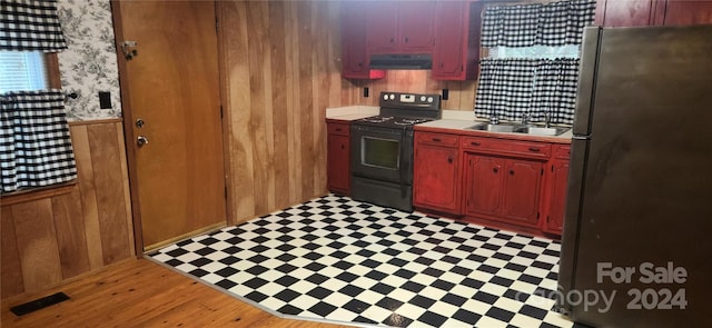 kitchen featuring black range, wooden walls, stainless steel fridge, sink, and light hardwood / wood-style floors