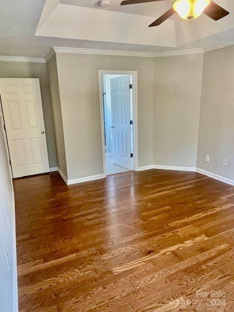 unfurnished room with ceiling fan, a raised ceiling, wood-type flooring, and ornamental molding