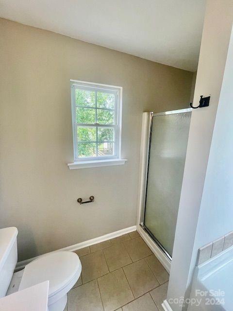 bathroom featuring tile patterned flooring, toilet, and a shower with door