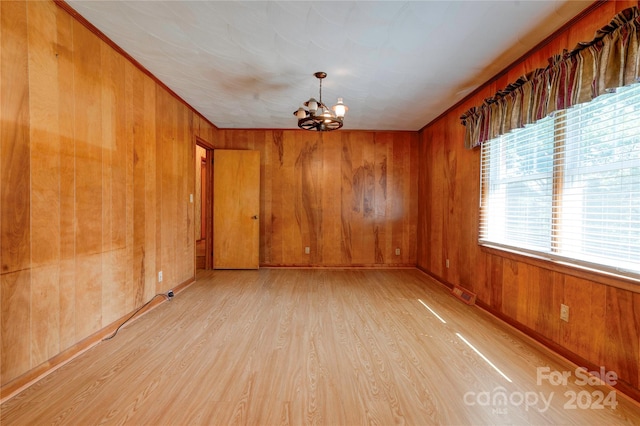 spare room featuring crown molding, light hardwood / wood-style flooring, a notable chandelier, and wooden walls