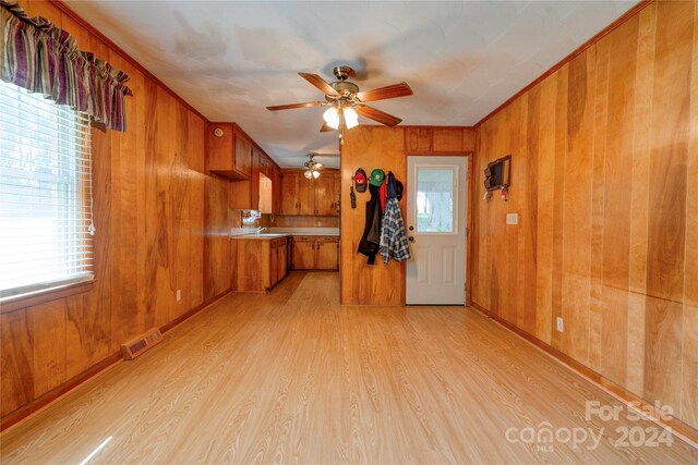 unfurnished living room with light wood-type flooring, ornamental molding, wood walls, sink, and ceiling fan