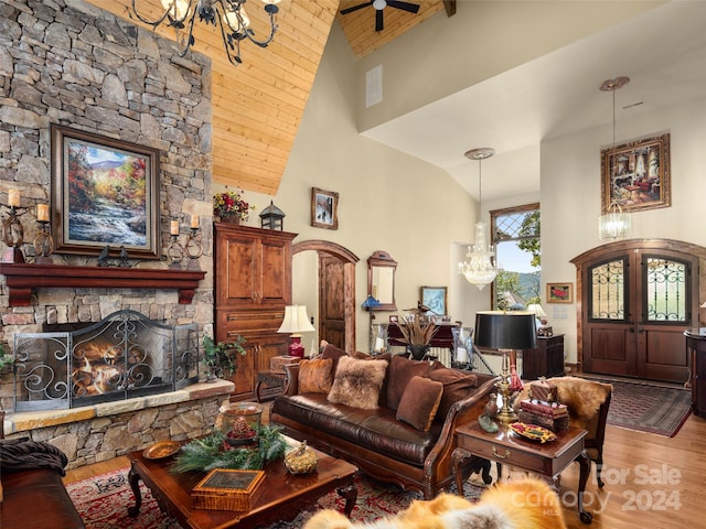 living room featuring ceiling fan with notable chandelier, light wood-type flooring, high vaulted ceiling, and a stone fireplace