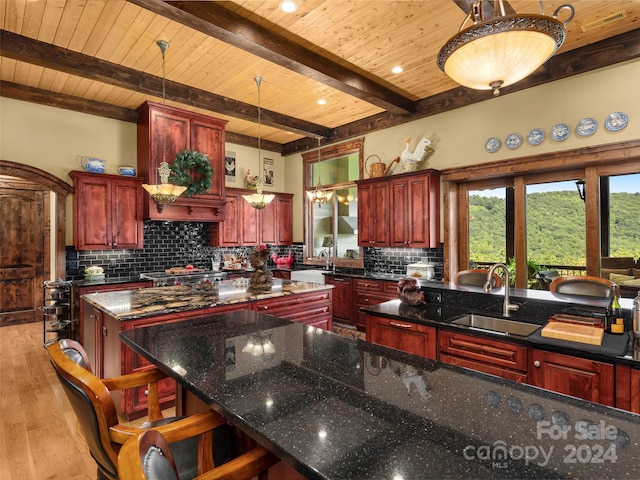 kitchen with hanging light fixtures, light hardwood / wood-style flooring, backsplash, a center island, and dark stone counters