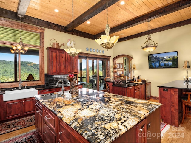 kitchen with backsplash, dark stone countertops, an inviting chandelier, and an island with sink