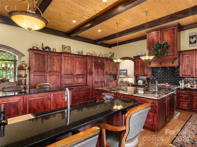 kitchen with dark stone counters, wood ceiling, a kitchen island with sink, tasteful backsplash, and hanging light fixtures