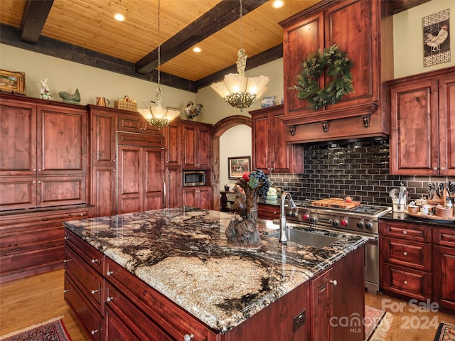 kitchen with built in appliances, dark stone counters, a kitchen island with sink, sink, and a chandelier