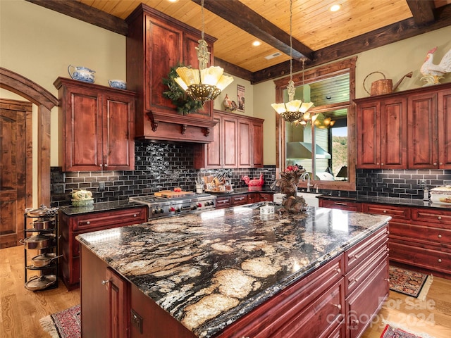 kitchen with beamed ceiling, hanging light fixtures, a chandelier, dark stone countertops, and light hardwood / wood-style floors