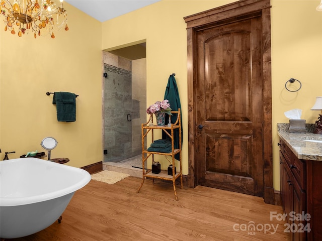 bathroom with an inviting chandelier, vanity, hardwood / wood-style floors, and plus walk in shower