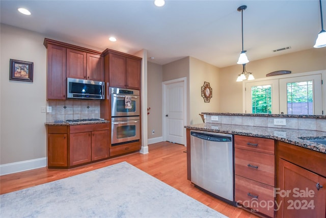 kitchen with light hardwood / wood-style floors, stainless steel appliances, hanging light fixtures, and light stone counters