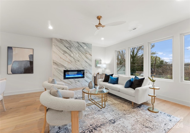 living room featuring light hardwood / wood-style floors, ceiling fan, and a premium fireplace