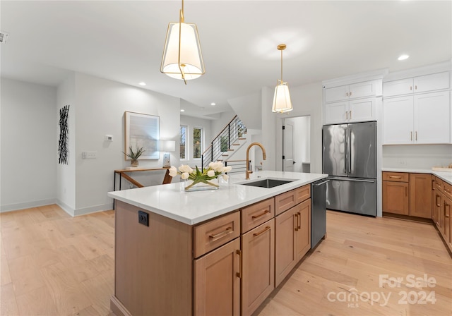 kitchen featuring white cabinetry, sink, hanging light fixtures, stainless steel appliances, and light wood-type flooring