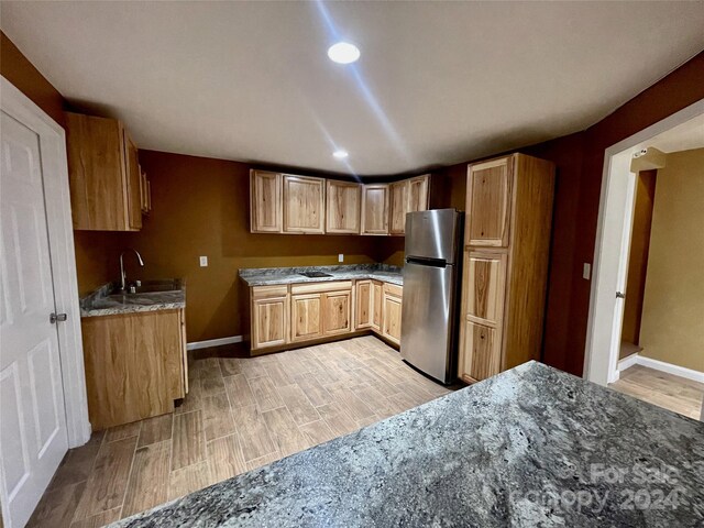 kitchen featuring light wood-type flooring, dark stone countertops, stainless steel refrigerator, and sink