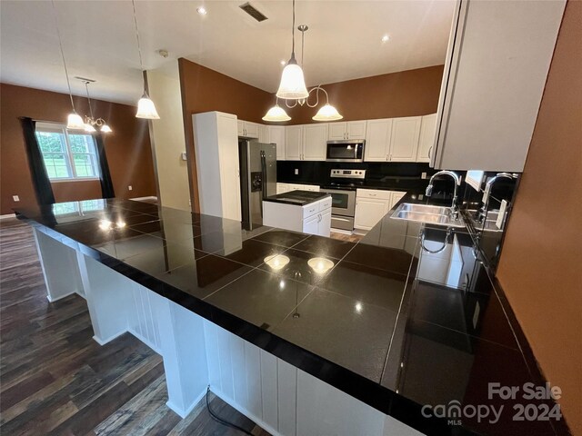 kitchen with dark hardwood / wood-style floors, appliances with stainless steel finishes, hanging light fixtures, sink, and white cabinets