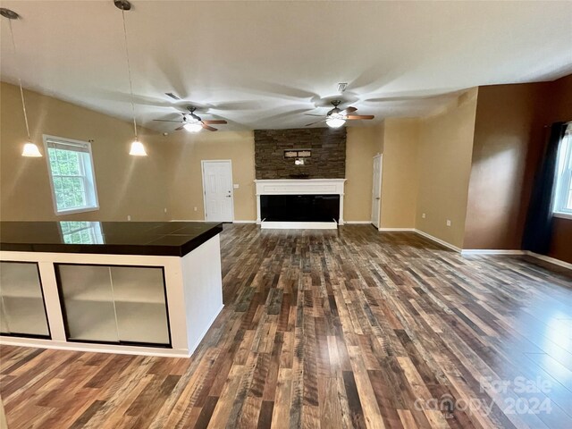 kitchen with dark wood-type flooring, ceiling fan, a stone fireplace, and hanging light fixtures