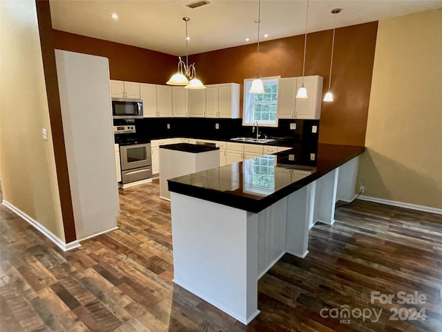 kitchen with white cabinetry, kitchen peninsula, dark wood-type flooring, hanging light fixtures, and appliances with stainless steel finishes