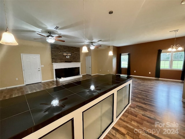 kitchen featuring a fireplace, ceiling fan with notable chandelier, decorative light fixtures, tile counters, and dark hardwood / wood-style floors