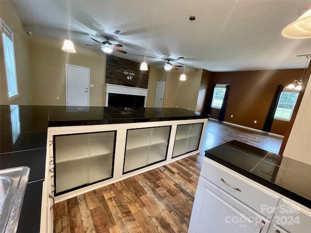 kitchen featuring dark hardwood / wood-style floors, ceiling fan with notable chandelier, tile counters, hanging light fixtures, and white cabinetry