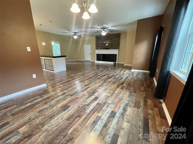 unfurnished living room with a large fireplace, ceiling fan with notable chandelier, and dark hardwood / wood-style flooring