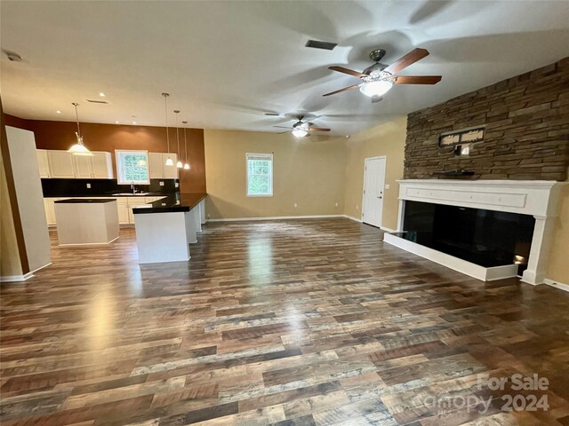 unfurnished living room featuring a healthy amount of sunlight, ceiling fan, dark hardwood / wood-style floors, and a stone fireplace