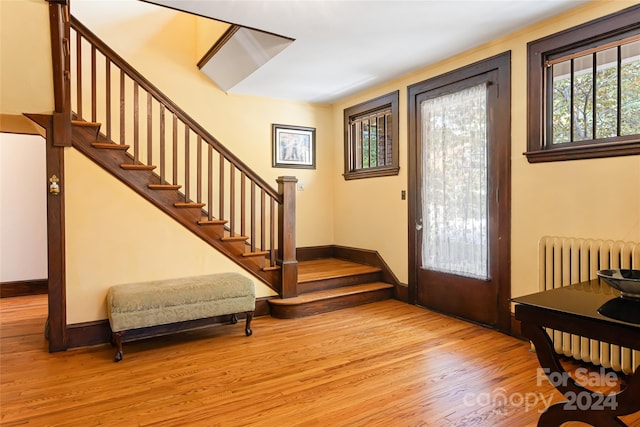 foyer entrance with wood finished floors, radiator heating unit, baseboards, and stairs