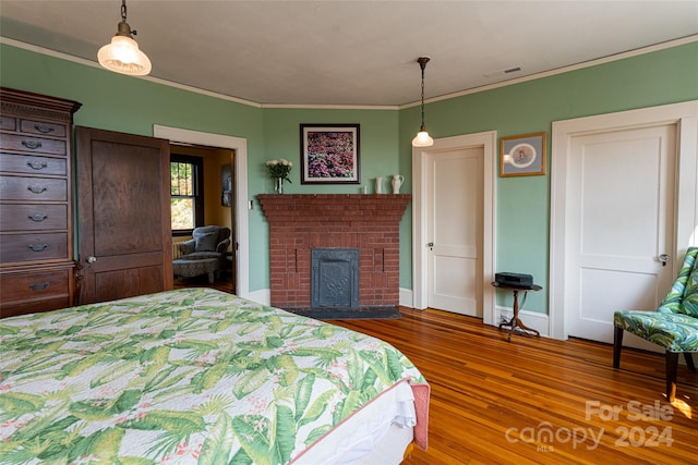 bedroom with ornamental molding, a brick fireplace, and hardwood / wood-style flooring